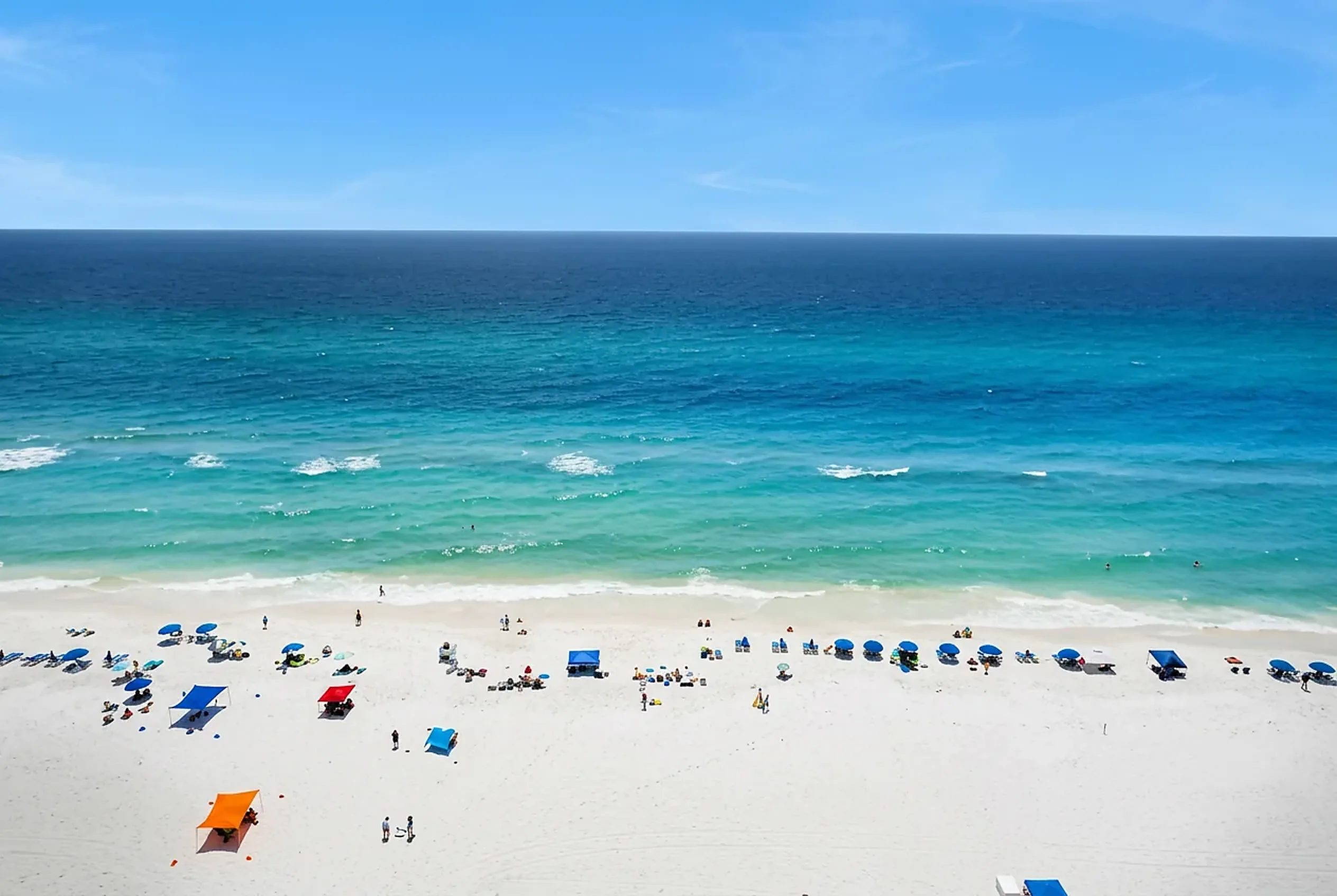 Emerald green gulf water and colorful umbrellas on a wide white sand beach in Florida
